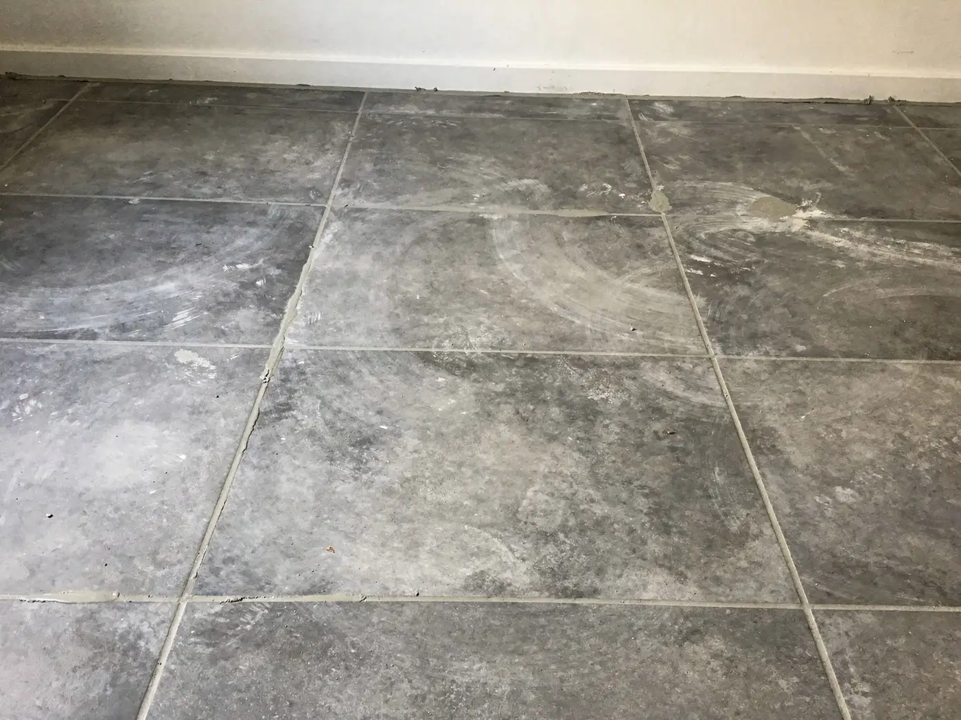 Voile blanc de ciment sur un carrelage neuf après la pose des joints