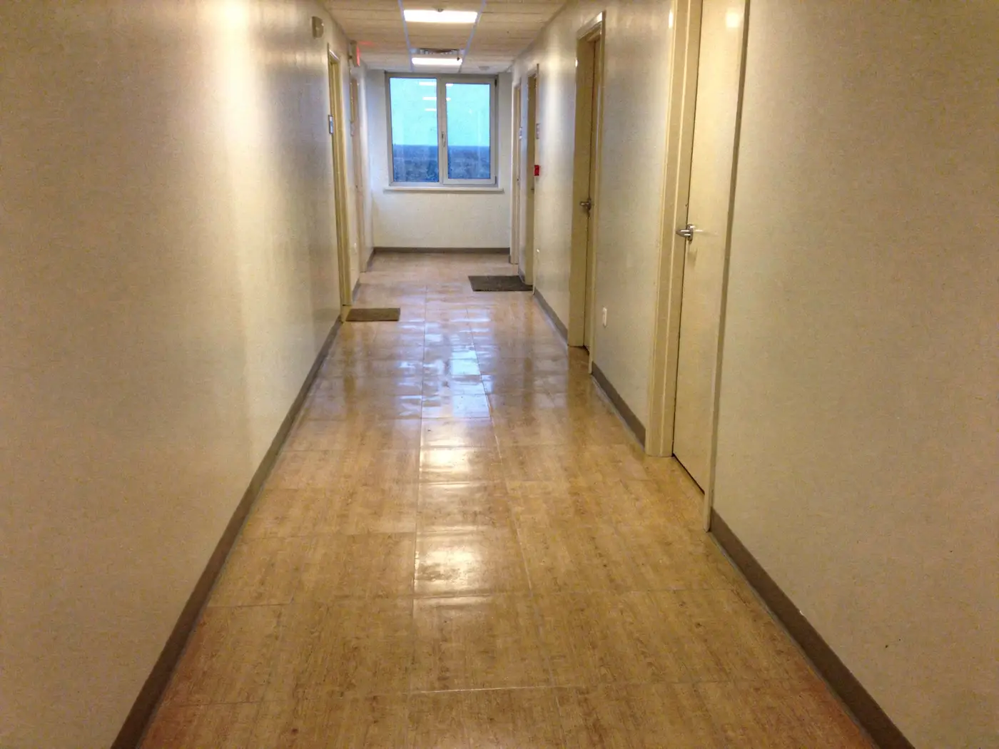 Couloir de bureaux vide à Lyon au petit matin, sol carrelé propre, encore légèrement humide